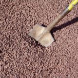 Pile of 3/8 inch red crushed stones with a shovel head resting on top