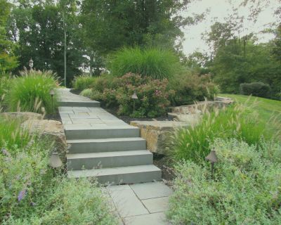 Stone steps leading through a landscaped garden with lush greenery, ornamental grasses, and flowering shrubs